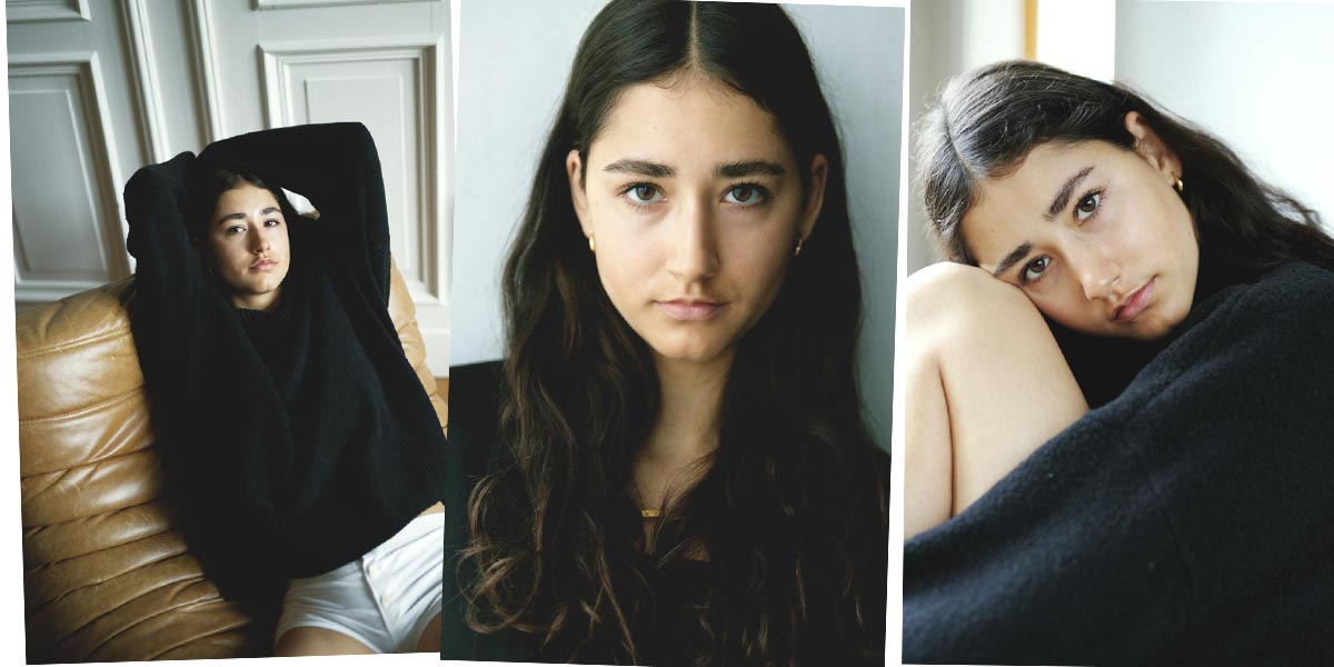 thumbnail--female-model-brown-curly-hair-berlin-white-pants-black-shirt-living-room-sitting-brown-couch
